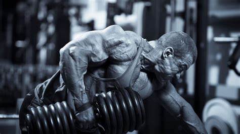 A bodybuilder demonstrating intense focus and strength while lifting heavy dumbbells in a gym.